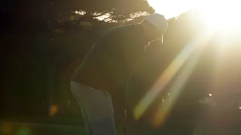 Golfspieler in gebeugter Haltung im Gegenlicht